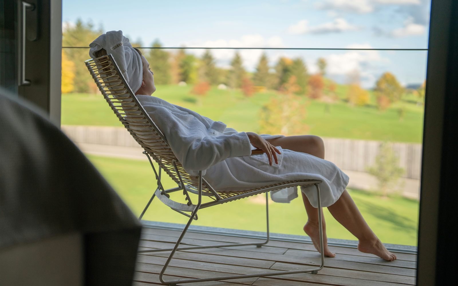 A woman in a robe stretched out on a balcony lounger looking over the course.