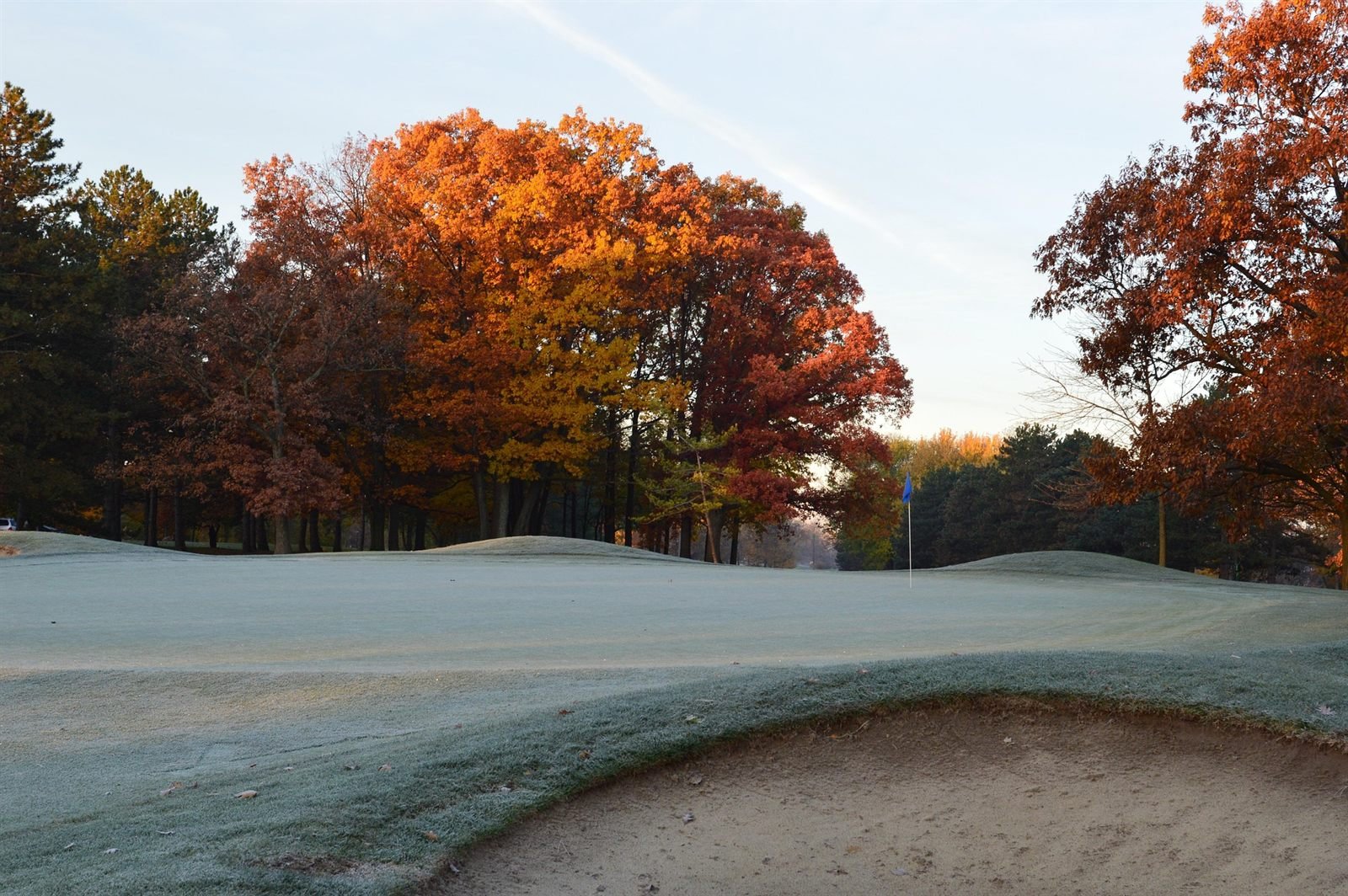 Frost lying across a bunker and the surrounding fairway, with trees in full autumn colour behind.