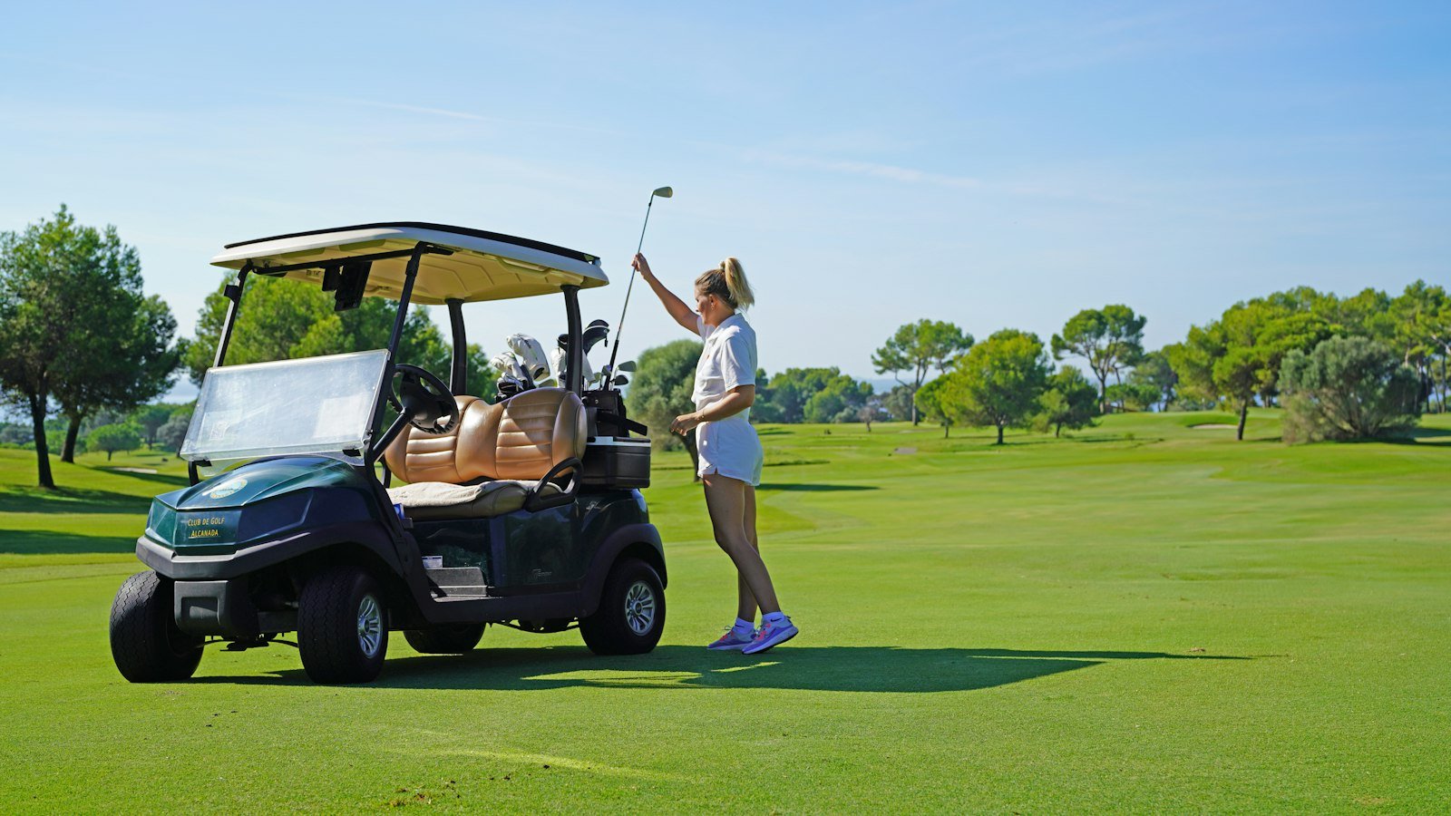A smiling golfer leaning over the wheel of a golf cart.