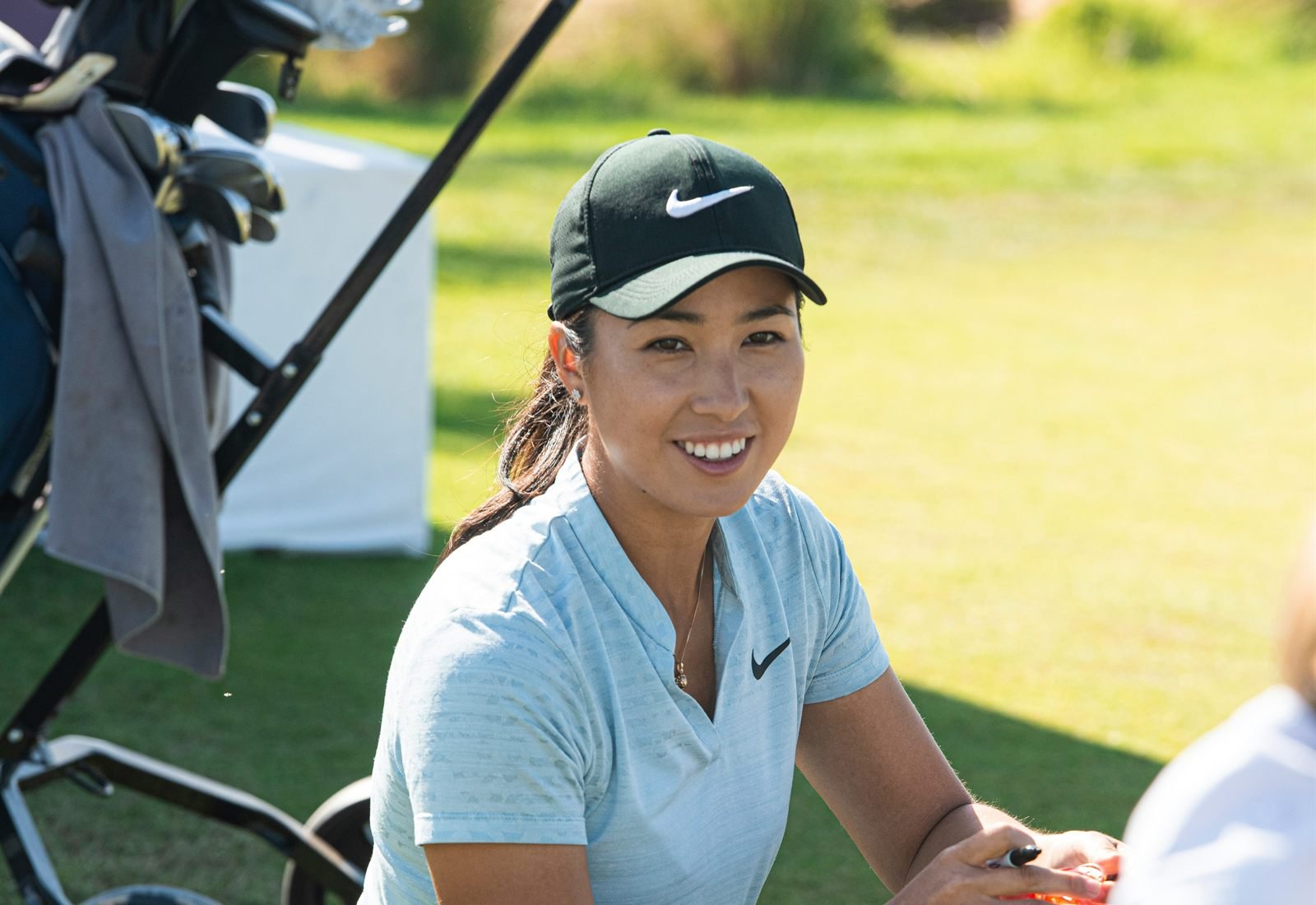 A smiling golfer crouched beside her bag on the course.