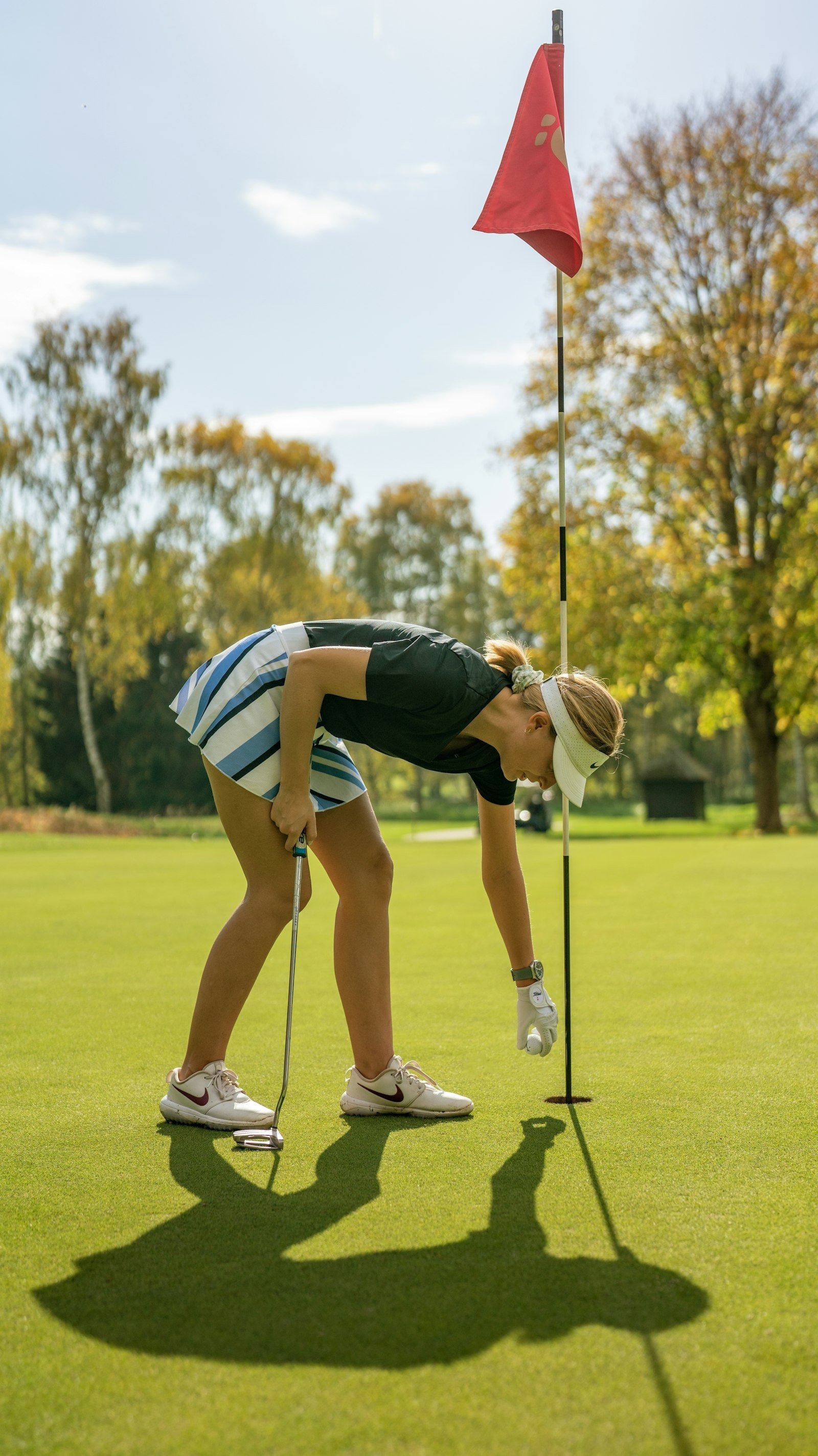 A golfer crouched behind her ball reading the line of a putt.