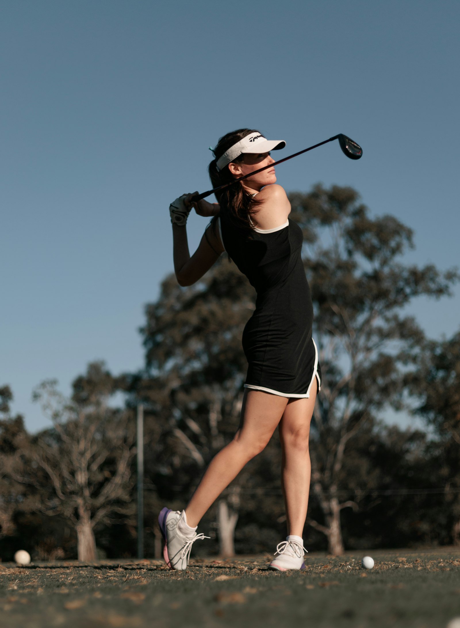 A golfer at the top of her backswing on an empty fairway.