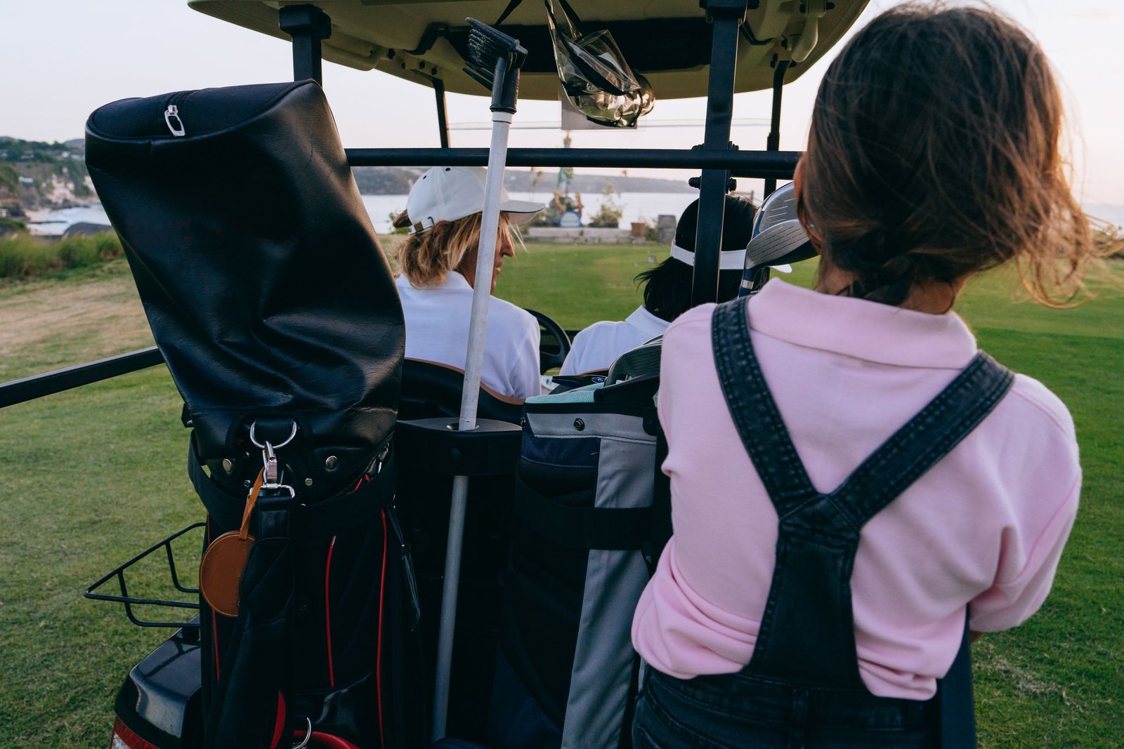 A group of women golfers riding out in a cart with their clubs on a coastal course at sunset.