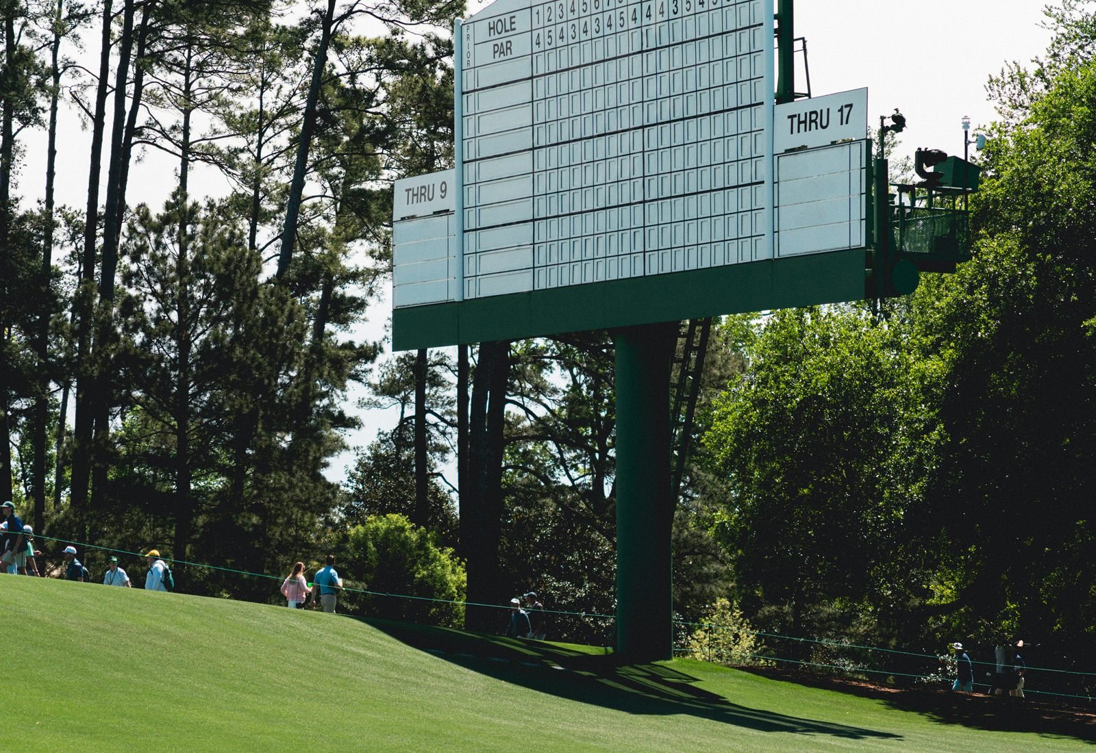 A tournament leaderboard standing tall beside the green, spectators watching below.