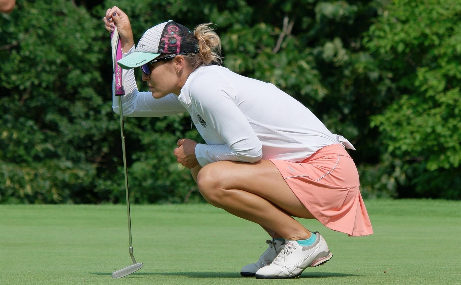 A woman crouched behind her ball on the green, reading the line of a putt.