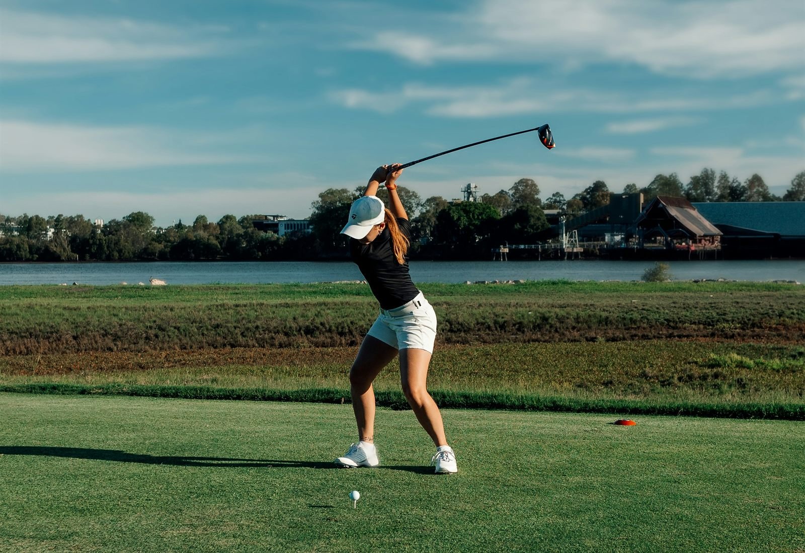 A woman driving from the tee, club at the top of her follow-through.